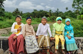 Five smiling young Muslim kids sitting on a brick wall